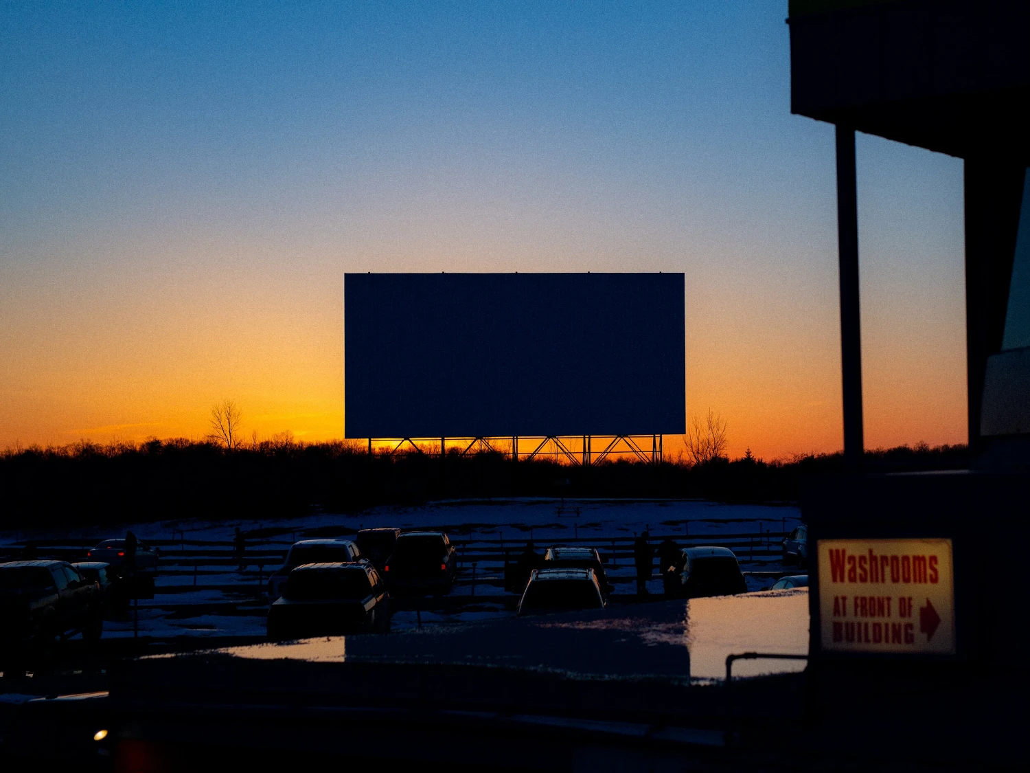 A drive-in cinema screen and parked cars at sunset