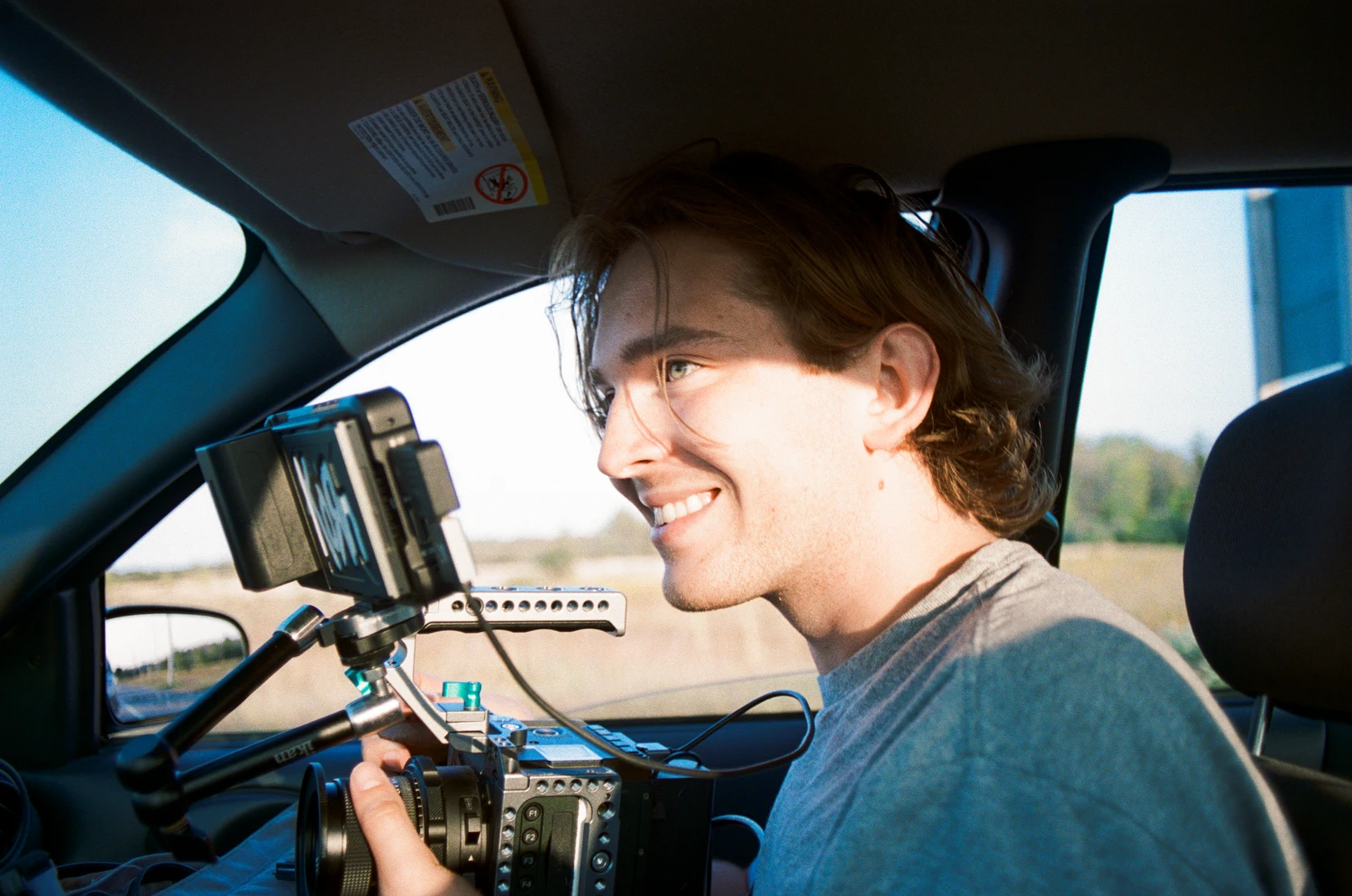 A smiling crew member holding a cinema camera inside a car
