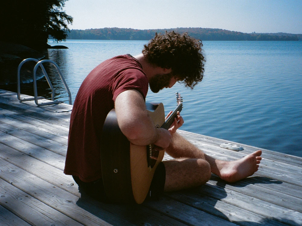 A man playing guitar on a dock beside the lake