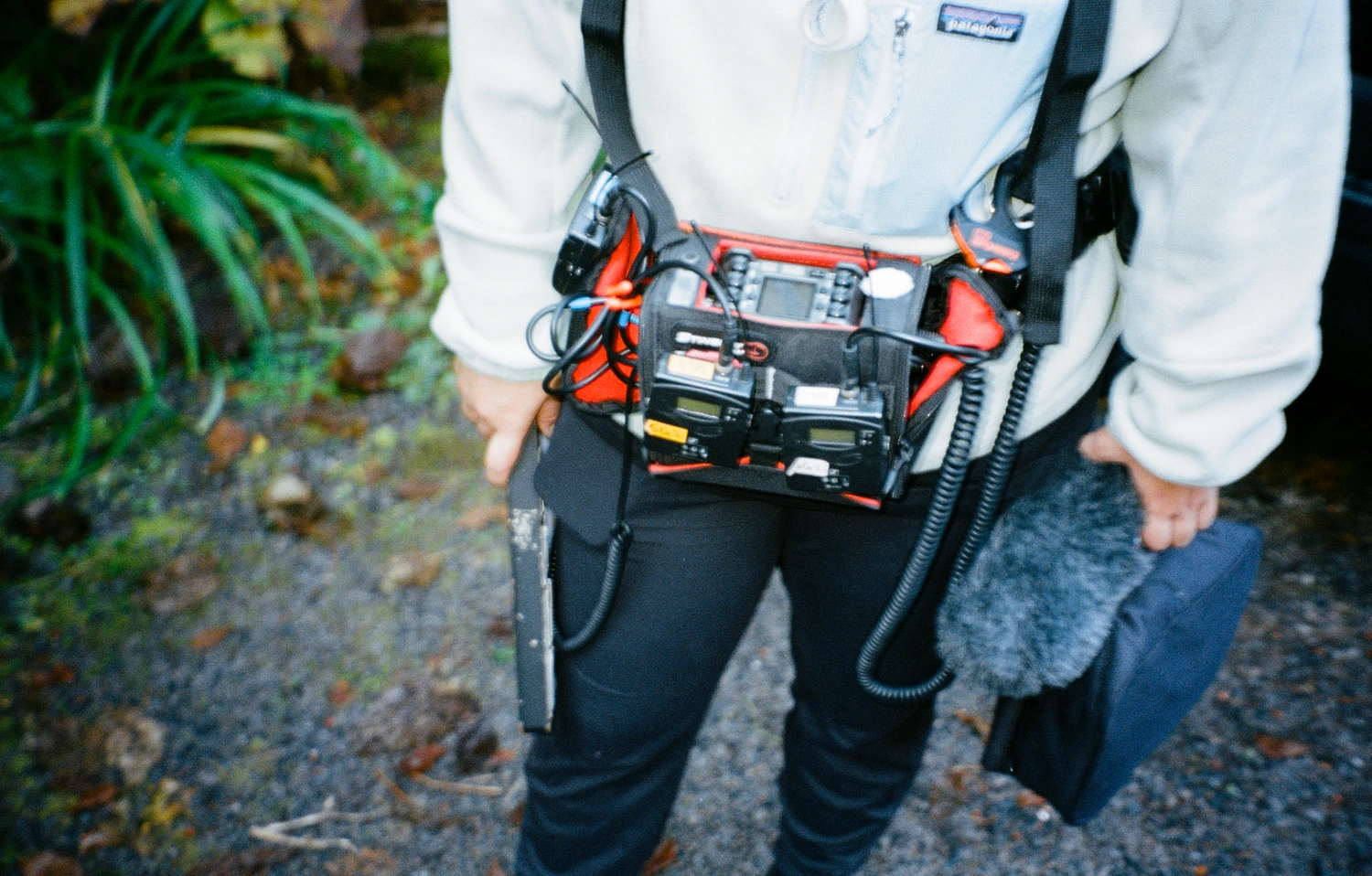 A crew member carrying a sound recorder and boom microphone